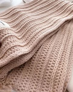 Close-up of cable knit wool scarf in soft mauve with textured fringes and woven label