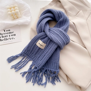 Blue twist knit wool scarf with elegant fringes and brand label on beige coat background