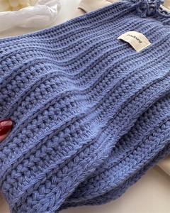 Detail of blue cable knit wool scarf showing thick ribbed texture and brand label
