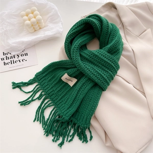 Deep green wool knit scarf with tassels and brand label on a beige blazer background