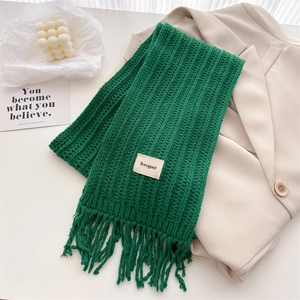 Detailed close-up of dark green cable knit wool scarf with brand label and long tassels
