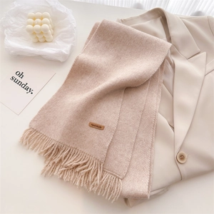 Close-up of beige knit scarf texture with handmade label and fringe detail