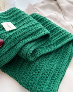 Close-up of grass green knit wool scarf featuring braided texture and a woven brand label