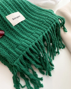 Close-up of dark green cable knit scarf with tassel details and white brand label