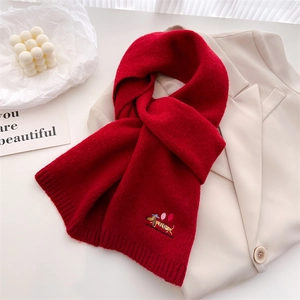 Close-up of red knitted scarf with colorful dachshund embroidery on beige suit fabric