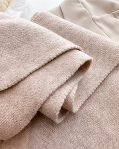 Close-up of soft thick knitted scarf texture with fringe detail in light beige