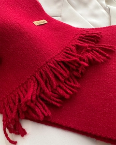 Detail of red knitted scarf with fringe and handmade leather label on beige coat