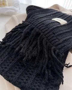 Close-up of black wool knit scarf showing thick cable texture and fringe tassels detail
