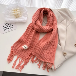 Flat lay of a coral pink knit scarf with fringe and a beige blazer on a white desk