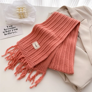 Detailed view of pink-orange wool knit scarf texture with fringe and woven brand label