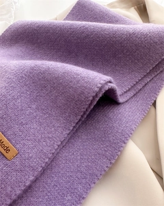 Detailed texture of thick dark purple knit scarf with a brown handmade leather label