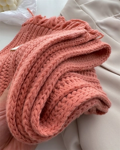 Detail of coral pink wool scarf featuring thick knit texture and fringe tassels