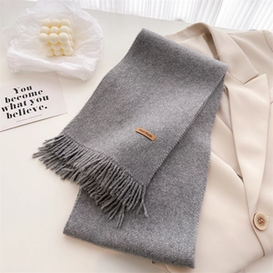 Detail of grey knitted scarf with soft fringe and brown handmade leather label