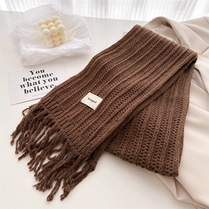 Detail of chunky dark brown knit scarf featuring fringe edges and a minimalist fabric label