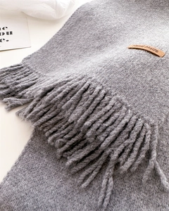 Close-up of grey knit scarf with long tassels and brown leather Hand Made label detail