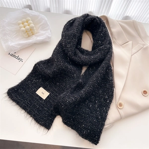 Close-up of black speckled wool knit scarf with tassel fringe and minimalist ins label