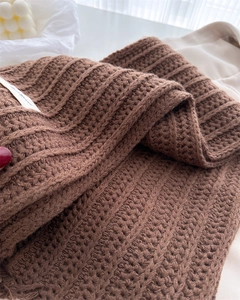 Close-up of brown wool scarf showing chunky cable knit texture and fabric label