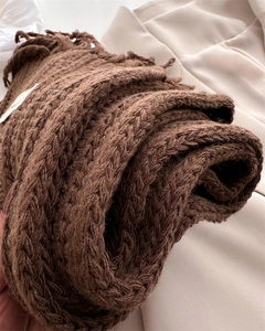 Macro detail of brown cable-knit wool scarf showing fringe edges and thick texture