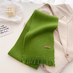 Close-up of grass green knit scarf with fringe and handmade leather label on beige blazer