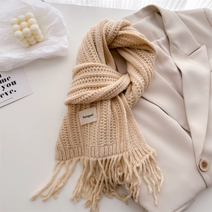 Detail of beige chunky knit wool scarf with tassel trim and woven label decoration