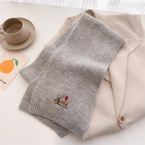 Detail of grey knitted scarf featuring colorful dachshund embroidery and soft texture