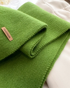 Detail of green knit scarf showing thick texture and handmade leather brand label