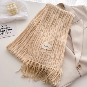 Detail of apricot cable knit scarf featuring fringe ends and a woven brand label