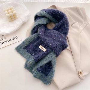 Blue-green gradient knit wool scarf laid on a beige blazer with a winter cozy aesthetic