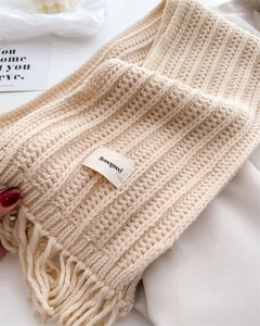 Detail of chunky knit beige wool scarf featuring soft fringe and woven brand label