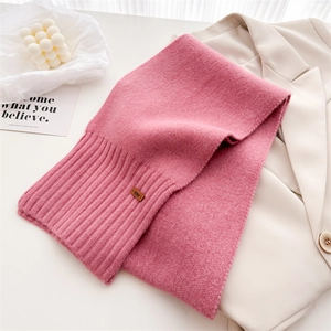 Nahaufnahme des rosa Strickschals aus Wolle mit Lederlogo auf beigem Sakko