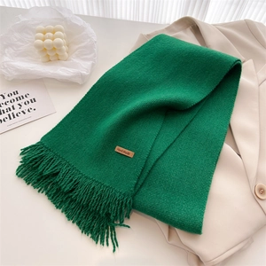 Close-up of emerald green knit scarf with hand made leather label and fringe tassels