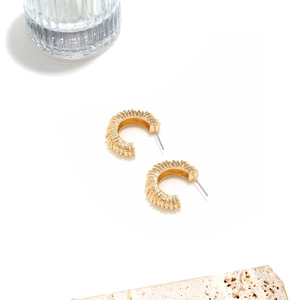 Détail de boucles d'oreilles dorées en forme de C avec des motifs en relief spirale