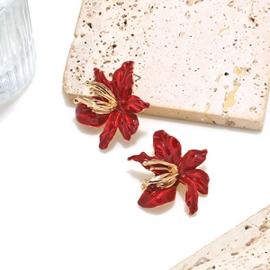 Detail view of red enamel flower earrings with golden stamens on stone background