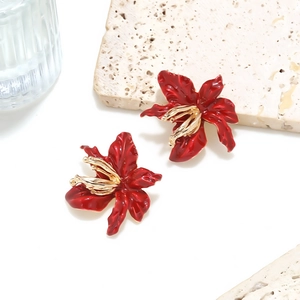 3D red enamel flower earrings with gold center set against a minimalist stone background