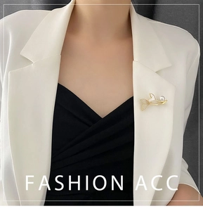 Close-up of a gold fishtail brooch with zircon pavé and white pearl on a blazer lapel