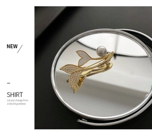 Macro shot of gold fish tail brooch with white zircon inlay and a round pearl detail