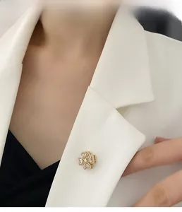 Detailed view of a golden rotating clover brooch with pavé zircon on a white blazer lapel