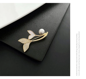 Detailed view of fish tail brooch with white shell, small diamonds and round pearl