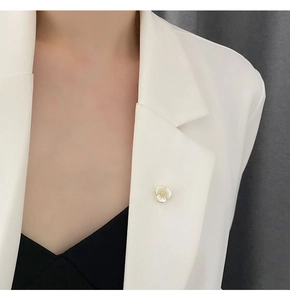 Close-up of a mini shell flower brooch pinned on a white blazer collar for a delicate look