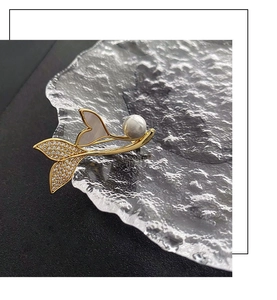 Close-up of golden whale tail brooch with mother-of-pearl, zircon and a pearl detail