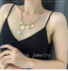 Close-up of a double-layered gold necklace with sun pendant and white pearls on a model