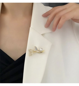 Close-up of golden mermaid tail brooch with pearl and zircons on white blazer