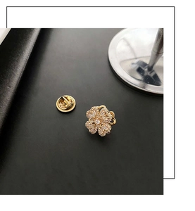 Close-up of gold flower brooch with white zircons and metal clasp on black background