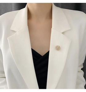 Detailed view of a rotating golden flower brooch with rhinestones on a white blazer