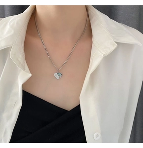 Detail einer silbernen Herz-Halskette mit LOVER Gravur, getragen zu einer Bluse