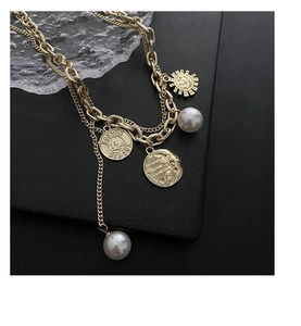 Macro detail of gold layered necklace with vintage coin pendant and white pearls
