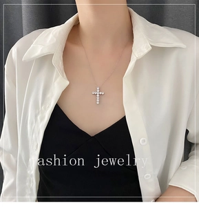Detail of silver cross pendant with pavé set crystals worn by a model on a thin chain