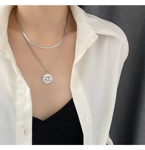 Detail of layered silver snake chain and coin pendant on a white shirt
