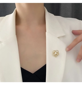 Détail de la broche camélia en perles avec design ajouré doré sur un revers de blazer