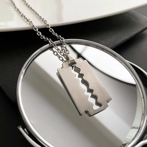 Collana con pendente a forma di lama in acciaio al titanio su superficie a specchio